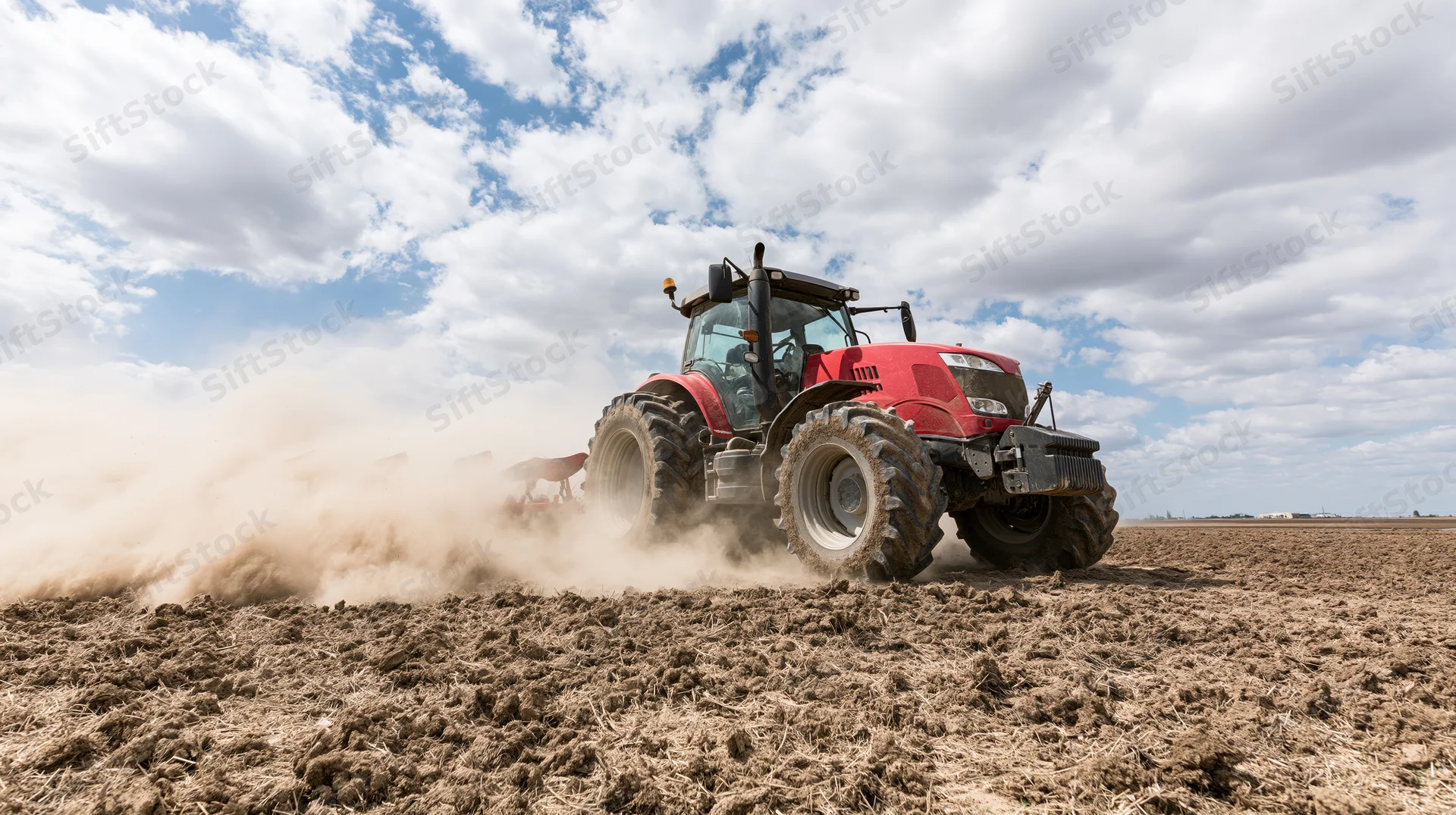 Red tractor plowing a dry field under a cloudy sky
