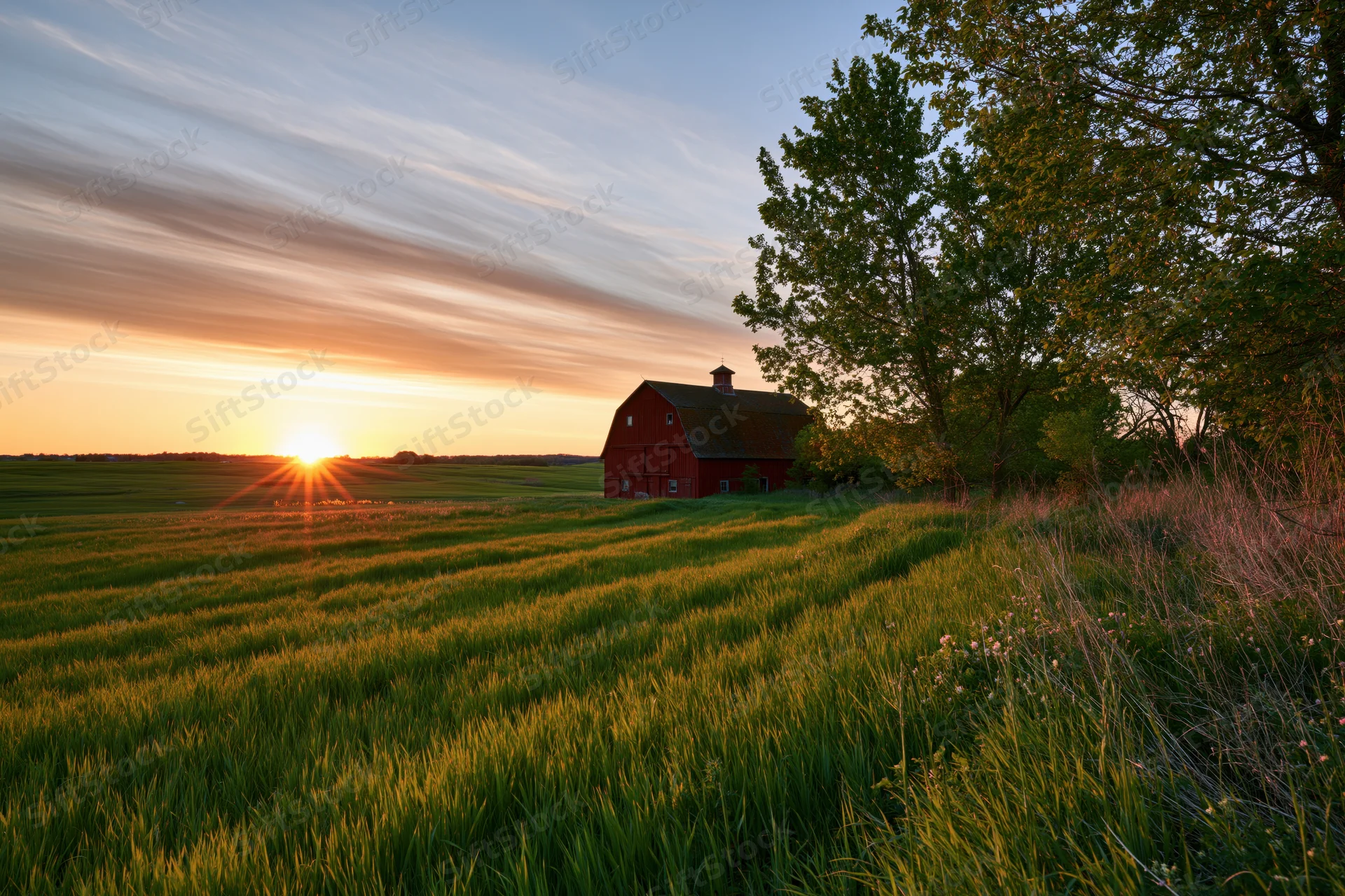 Red barn in a wide open farm field at sunset
