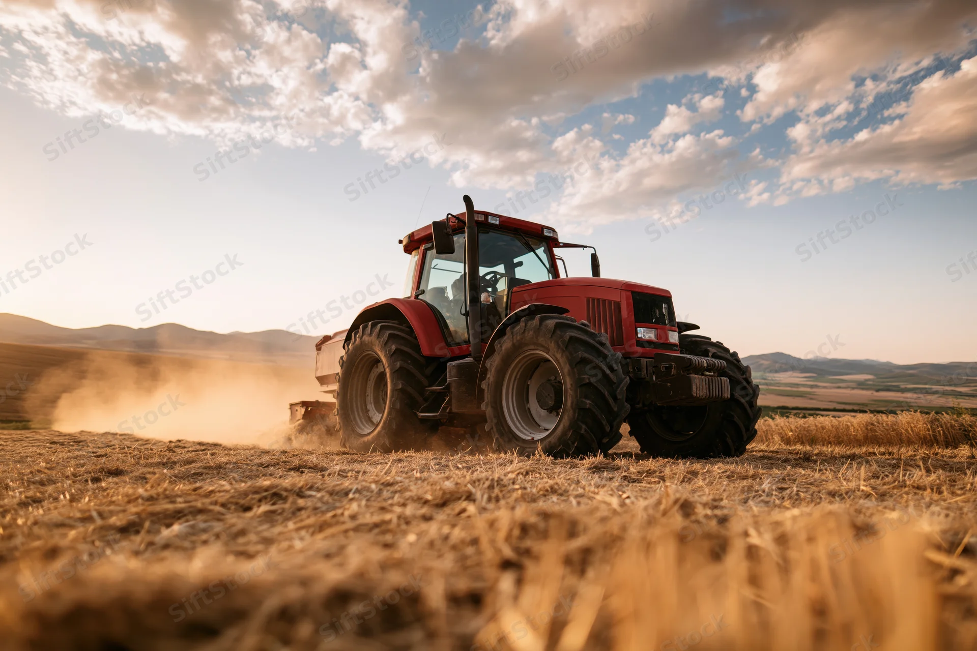 Red tractor harvesting wheat field kicking up dust trail