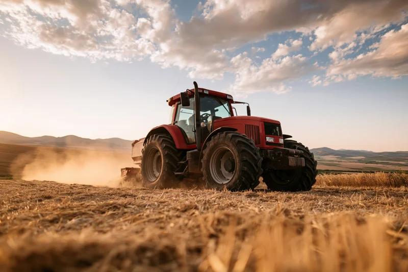 Red tractor harvesting wheat field kicking up dust trail