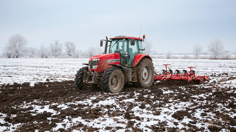 Red tractor pulling tillage equipment across a snow-covered field in winter