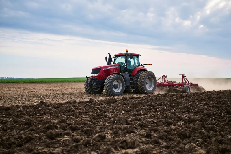 Red tractor pulling cultivator across tilled field