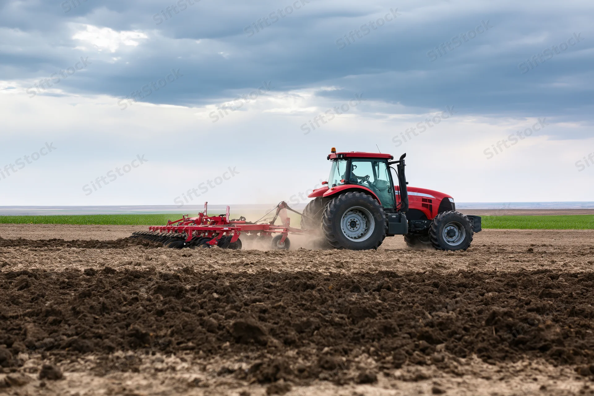 Red tractor pulling cultivator across tilled field