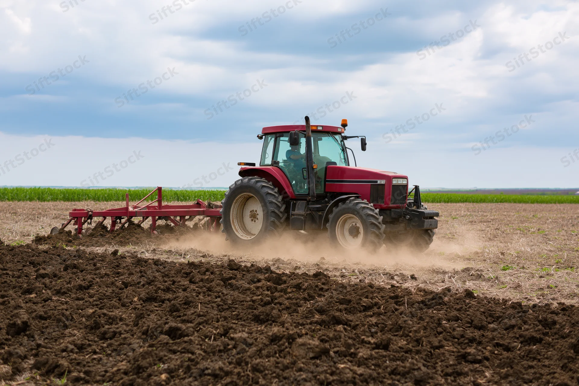 Red tractor pulling cultivator across tilled field