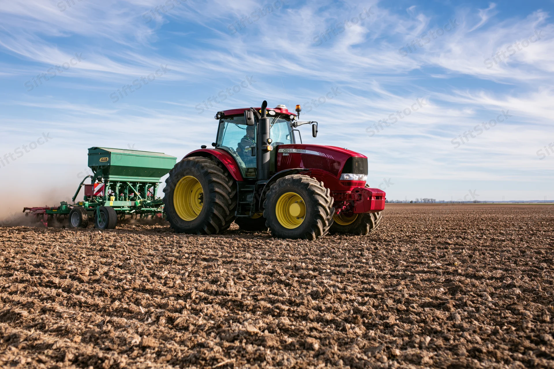 Red tractor pulling seed drill across plowed field
