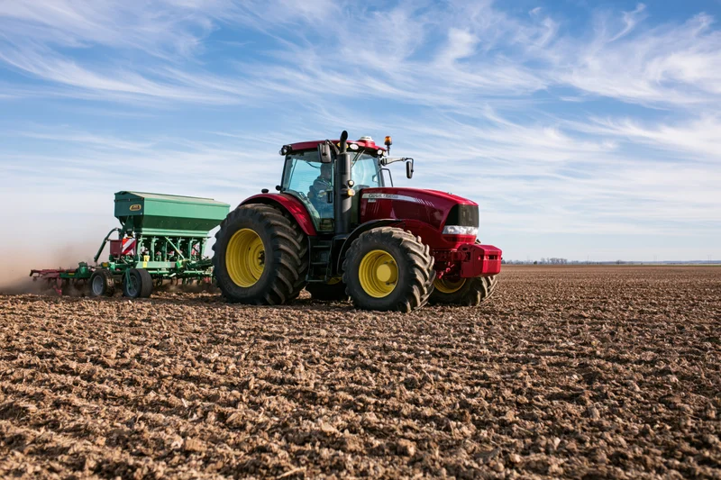 Red tractor pulling seed drill across plowed field
