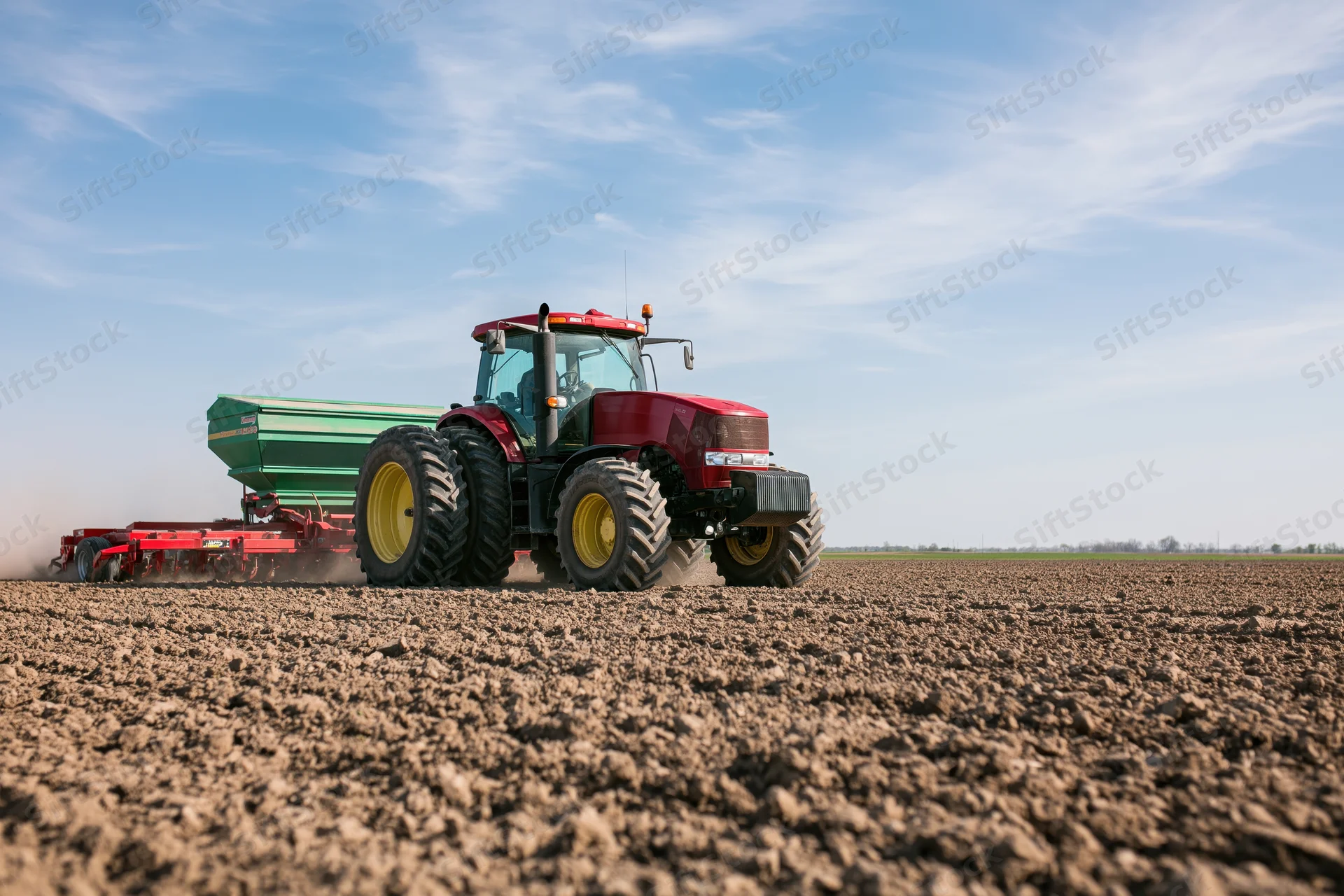 Red tractor pulling seed drill across freshly plowed field