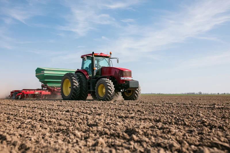 Red tractor pulling seed drill across freshly plowed field