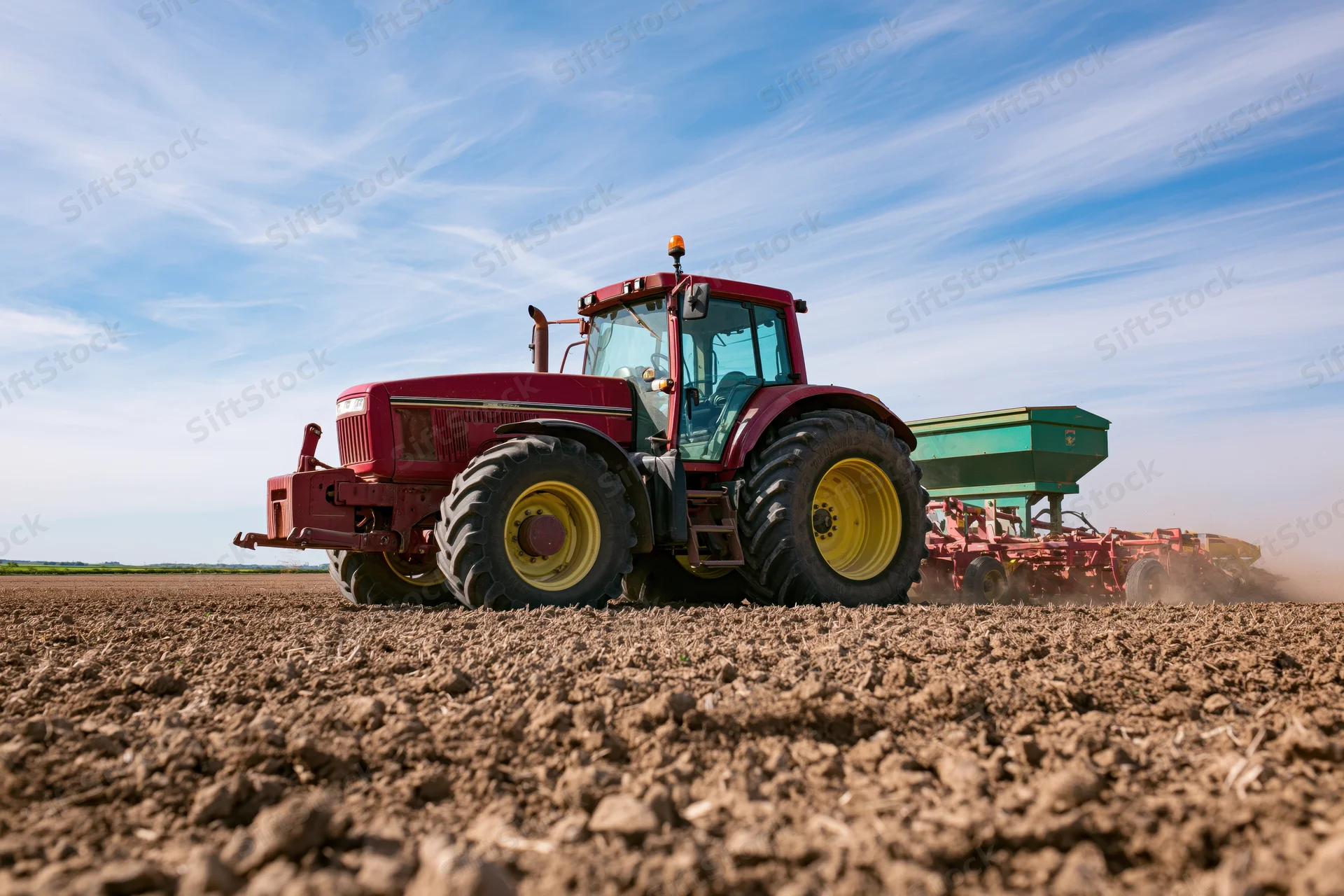 Red tractor pulling seed drill across freshly plowed field