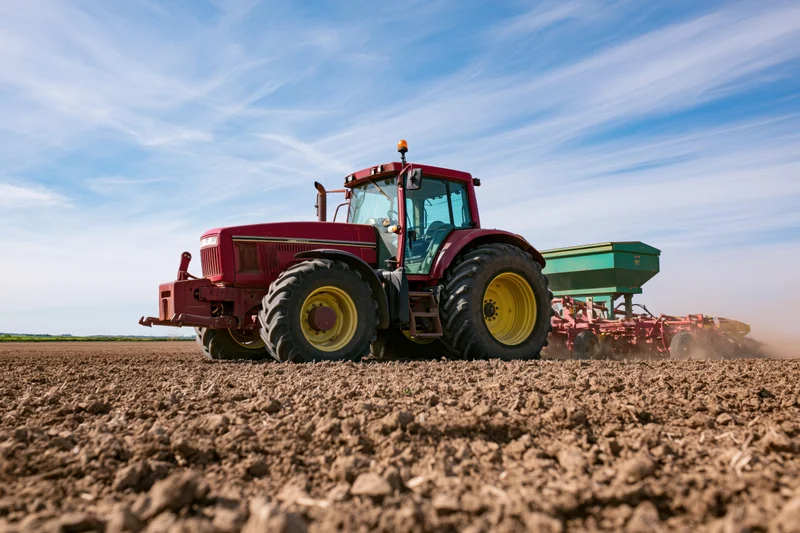 Red tractor pulling seed drill across freshly plowed field