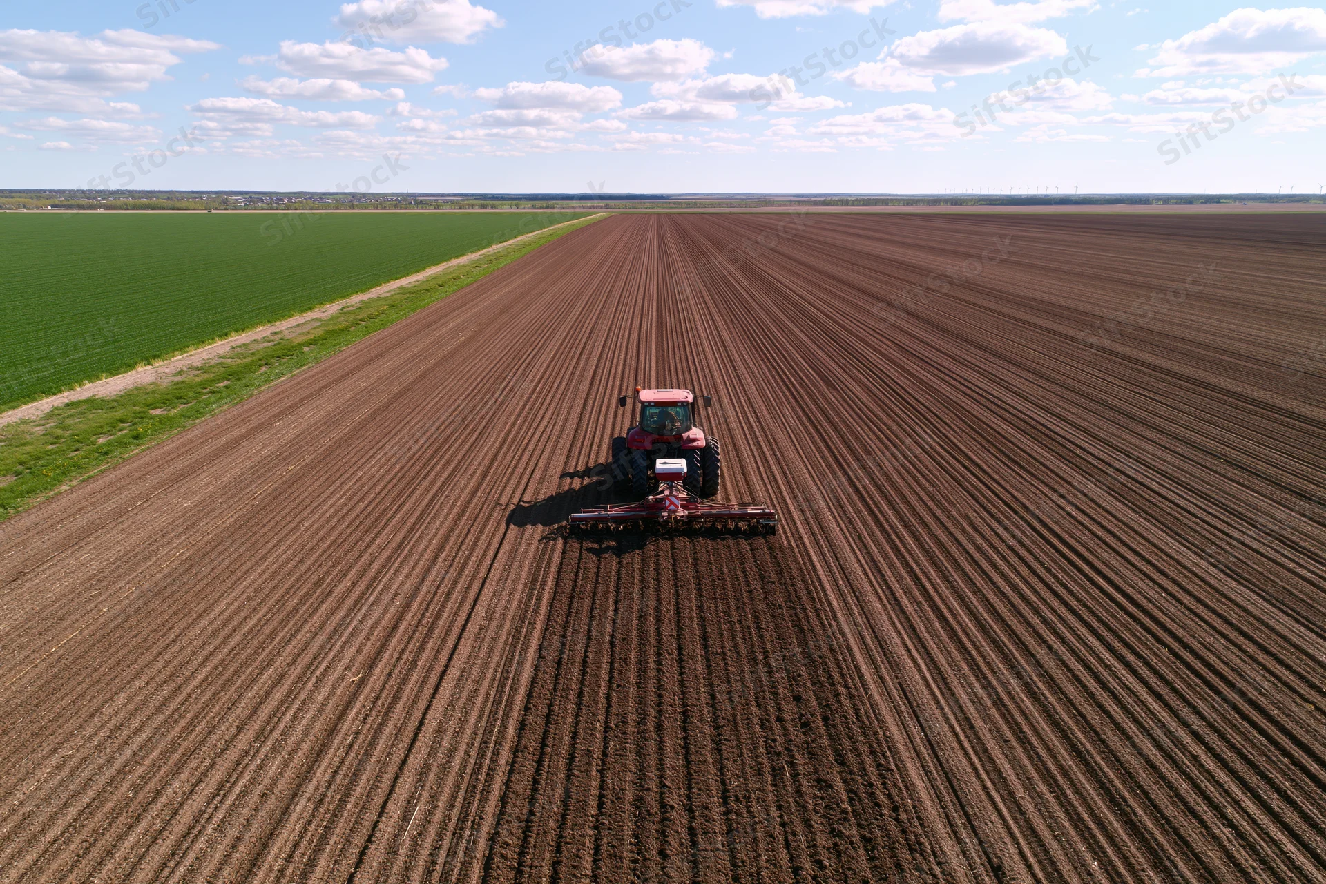 Red tractor pulling seeder across freshly plowed agricultural field under partly cloudy sky