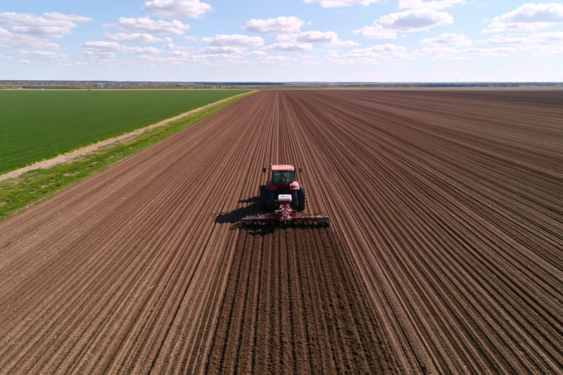 Red tractor pulling seeder across freshly plowed agricultural field under partly cloudy sky