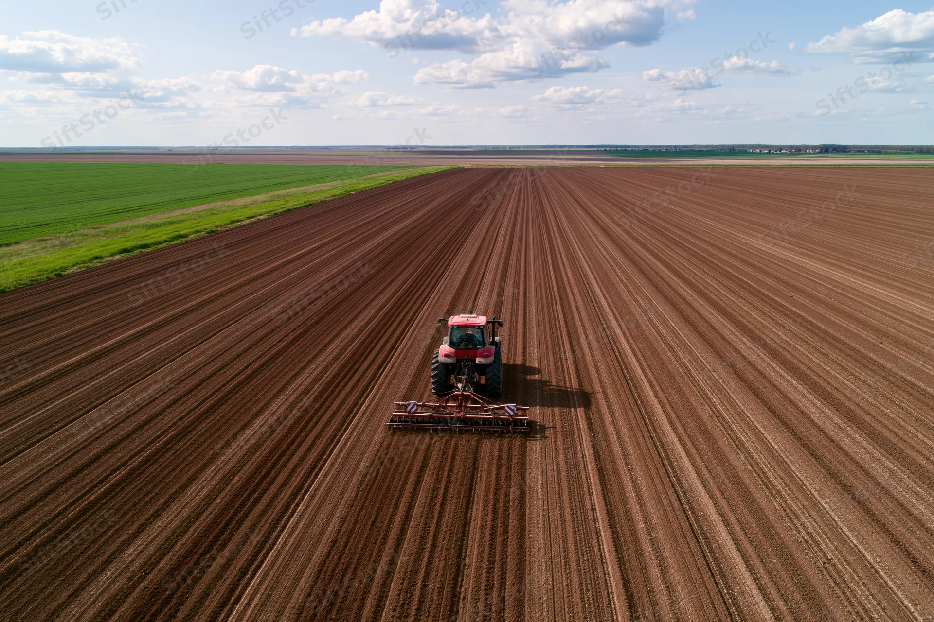 Red tractor pulling seeder across large freshly plowed field