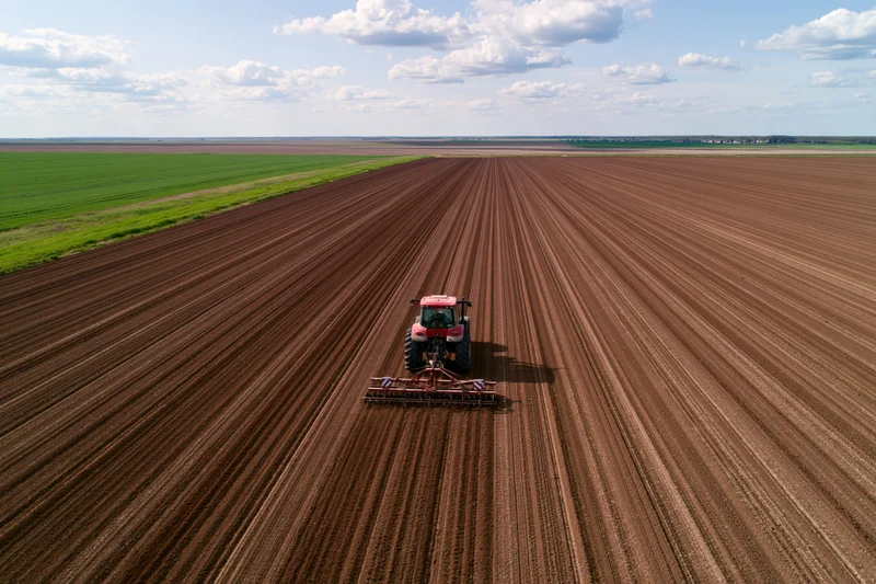 Red tractor pulling seeder across large freshly plowed field