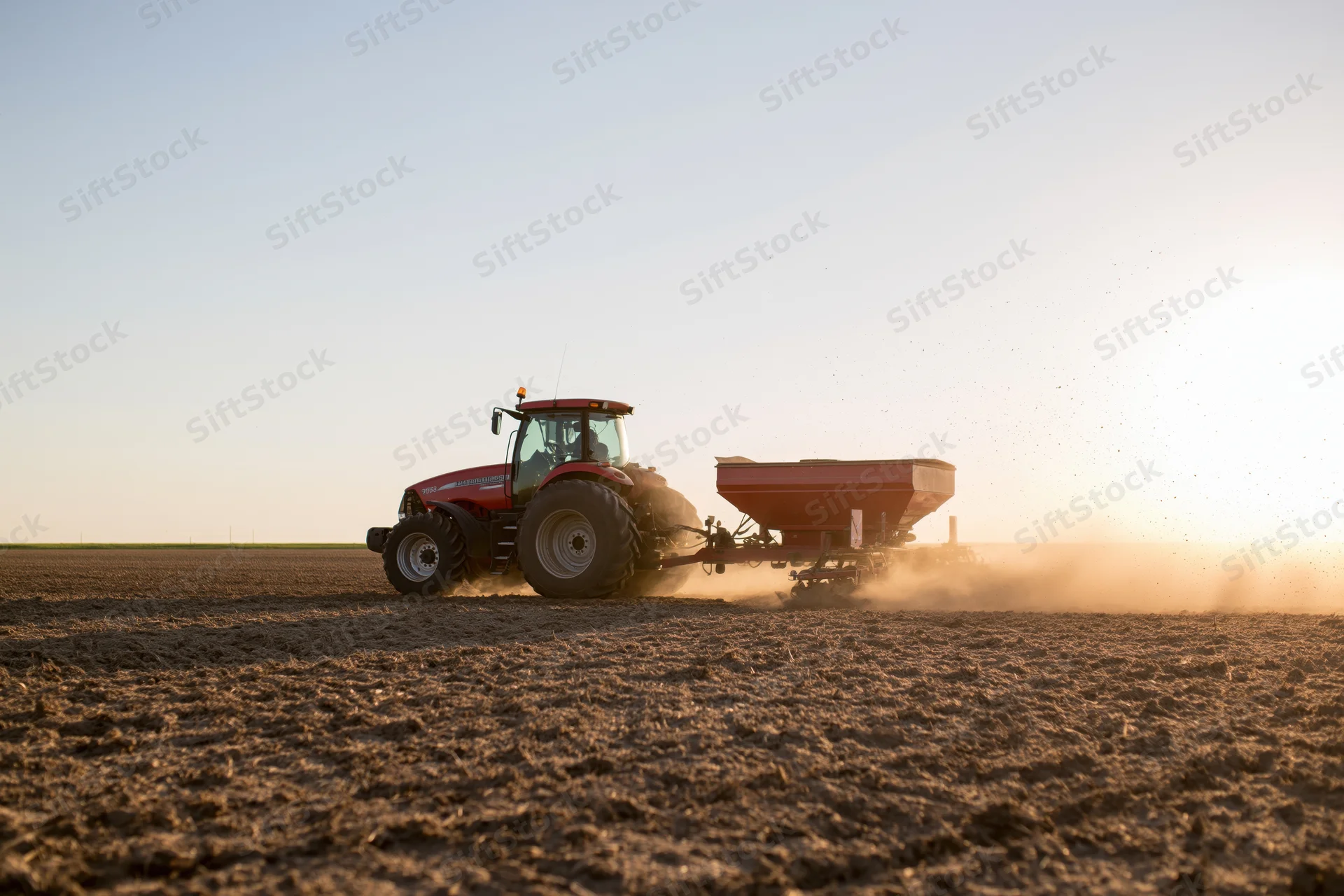 Red tractor pulling spreader across plowed field at sunset