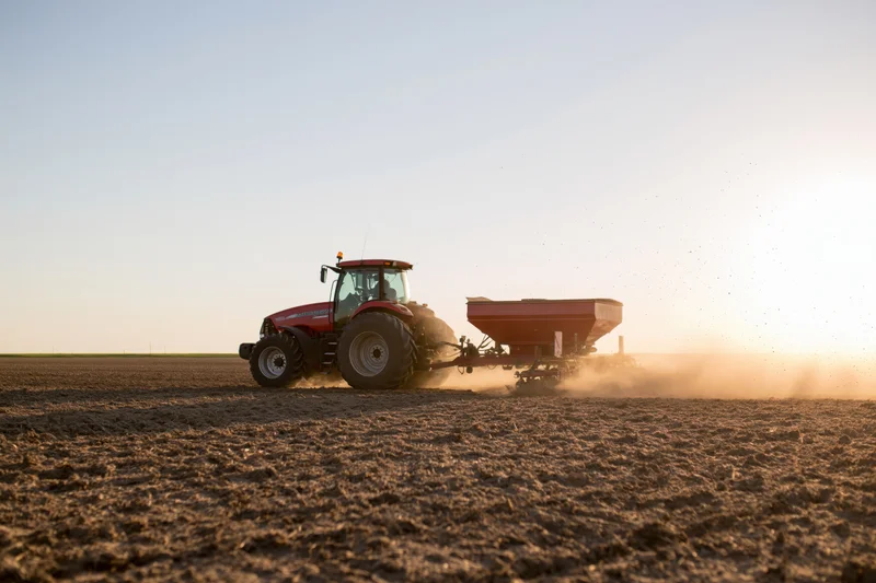 Red tractor pulling spreader across plowed field at sunset