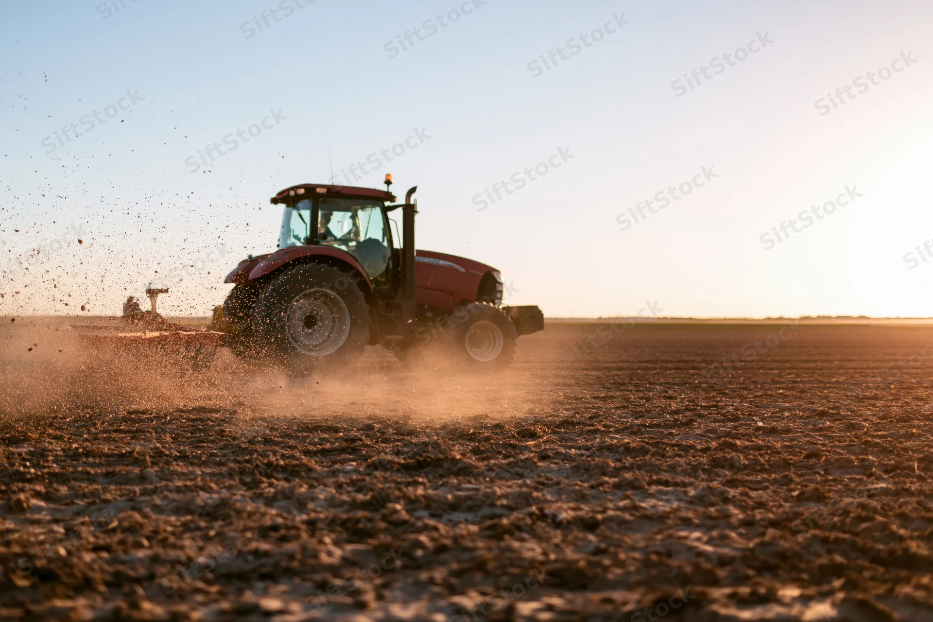Red tractor pulling spreader attachment across freshly plowed field at sunset