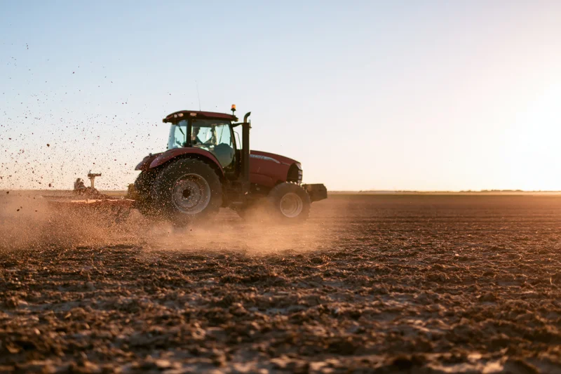 Red tractor pulling spreader attachment across freshly plowed field at sunset