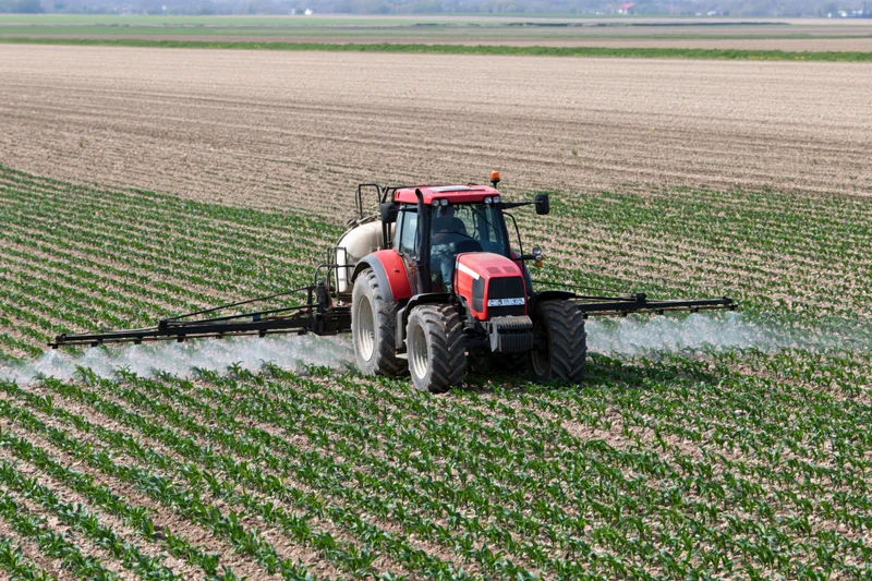 Red tractor spraying crops in a field
