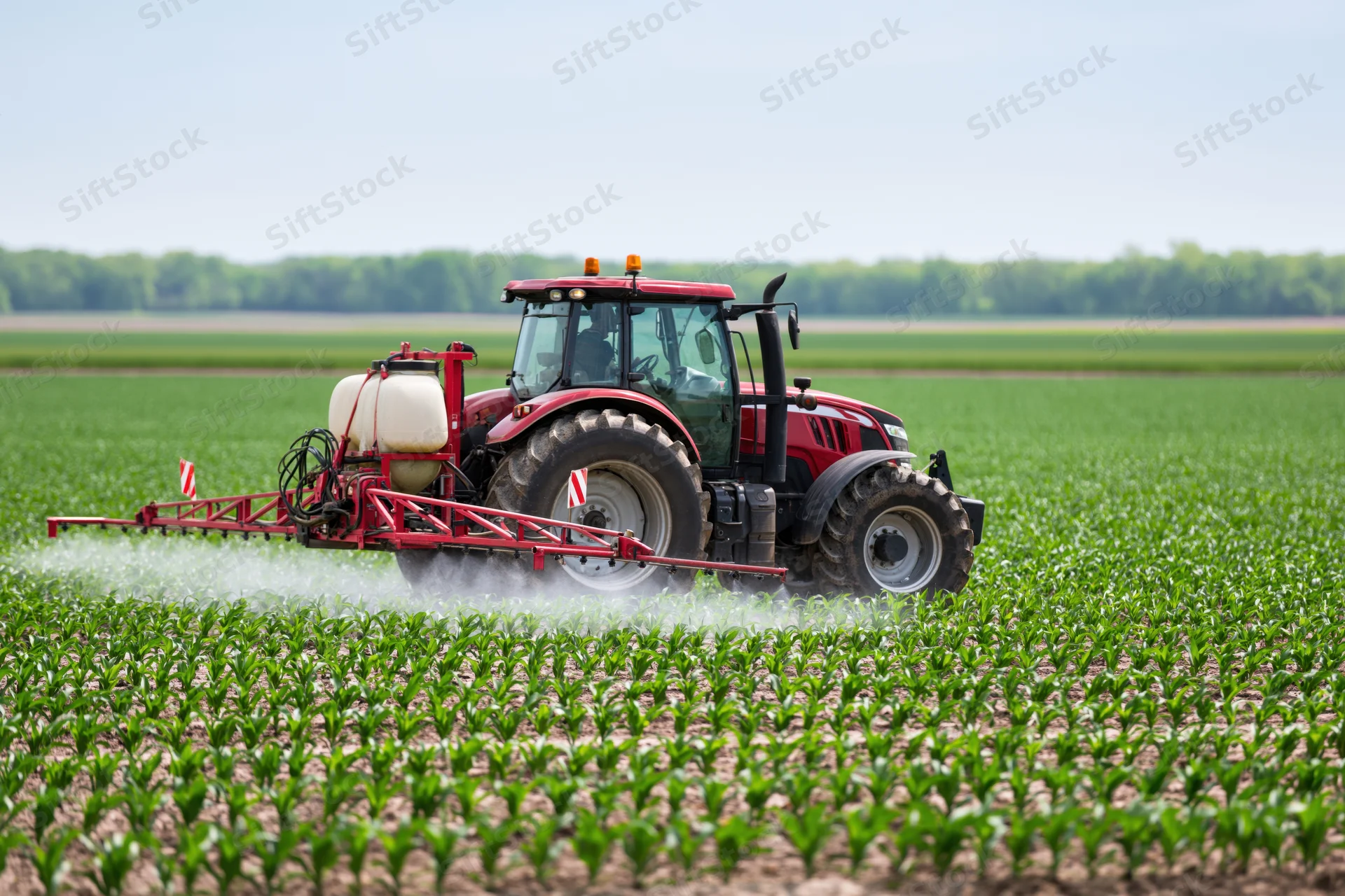 Red tractor with rear-mounted sprayer moving across a green crop field