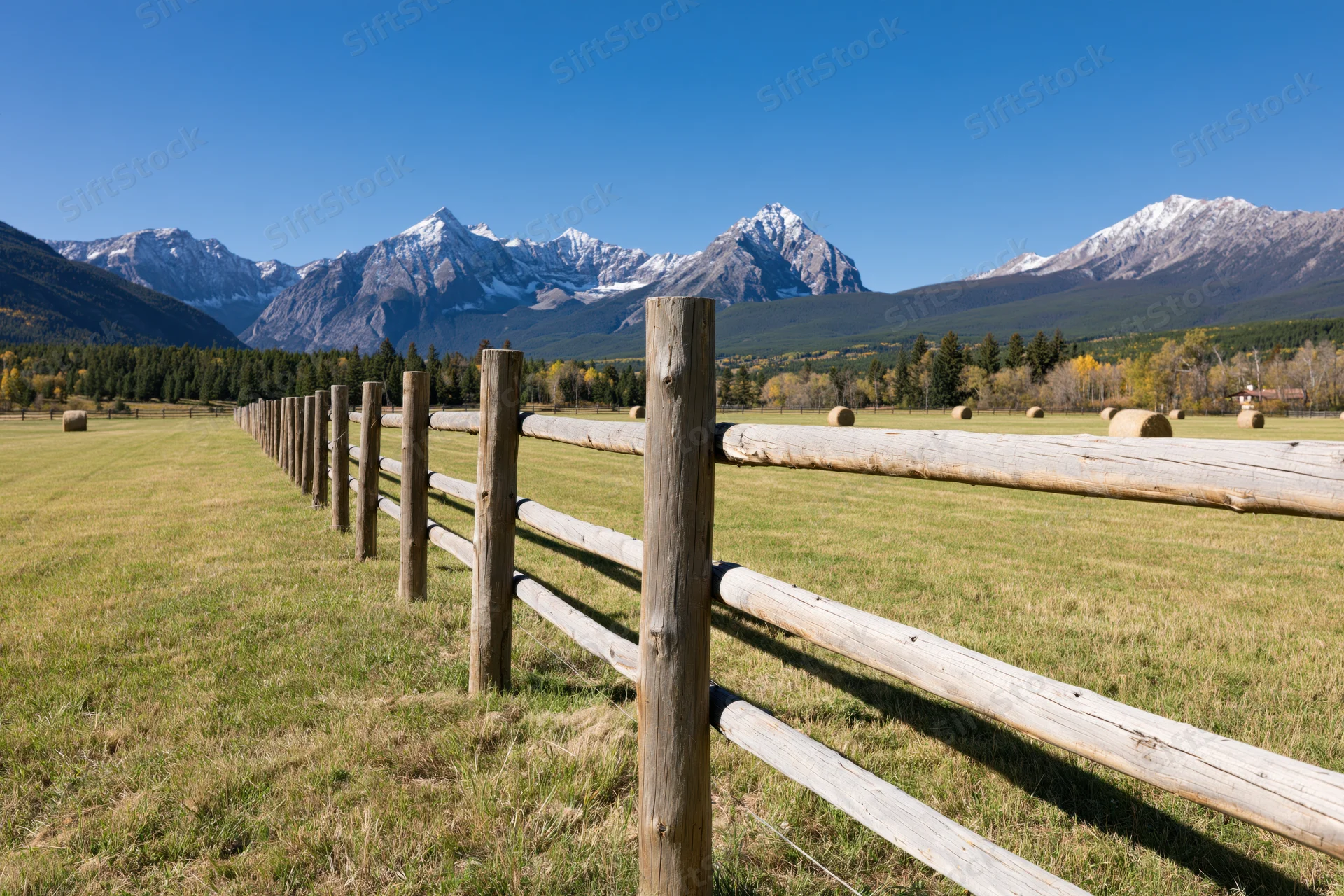 Wooden fence running diagonally across a grassy field with snow-capped mountains in the background