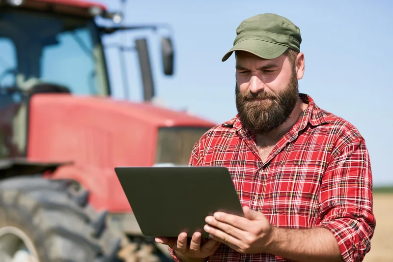 Bearded man using tablet in field with tractor in background