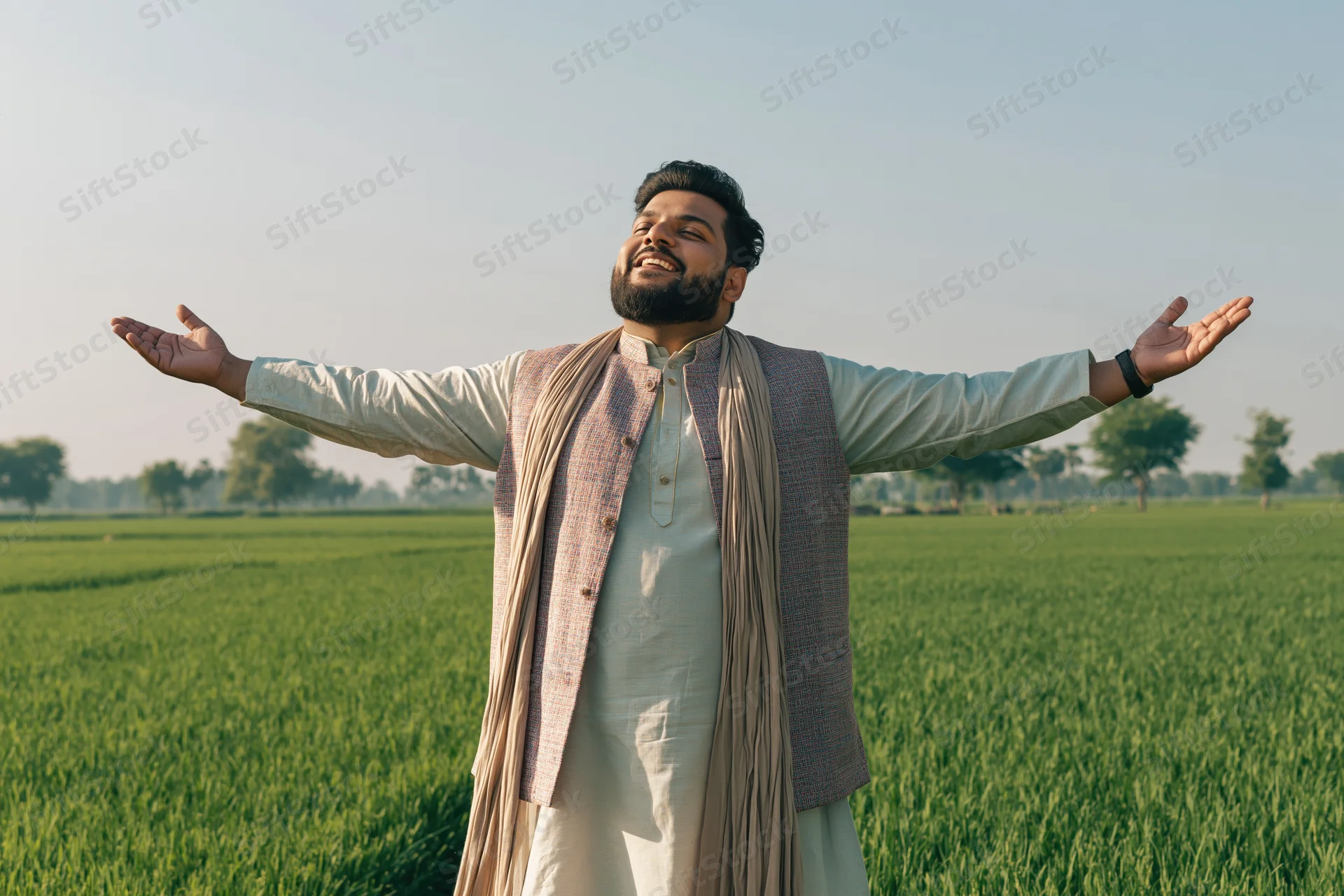Man with arms open smiling in a green rice field