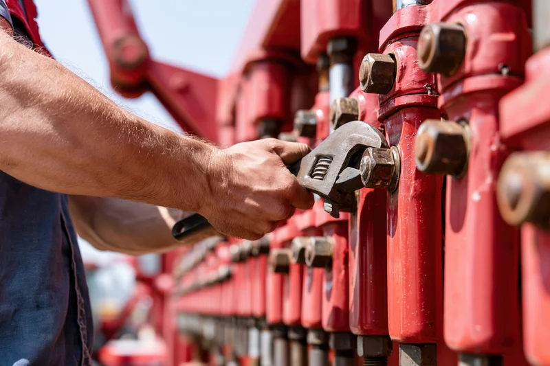 Mechanic tightening bolt on red farm machinery with wrench outdoors