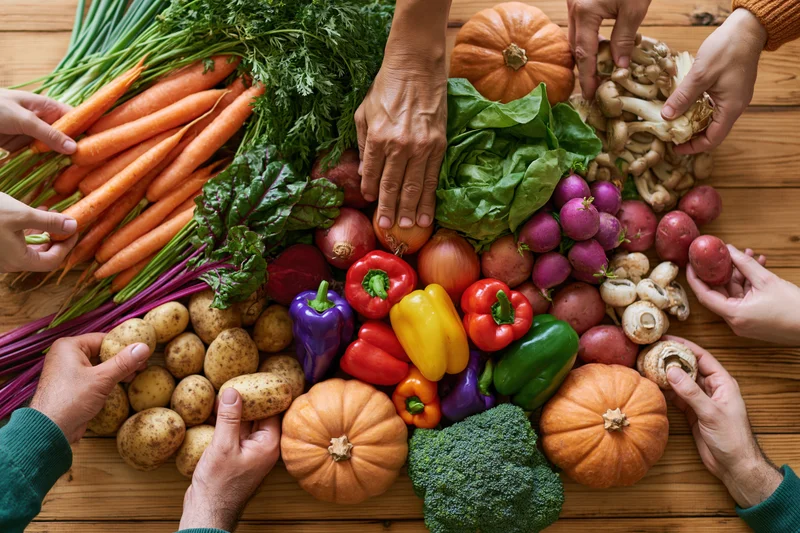 Hands reaching for fresh vegetables arranged on a wooden table