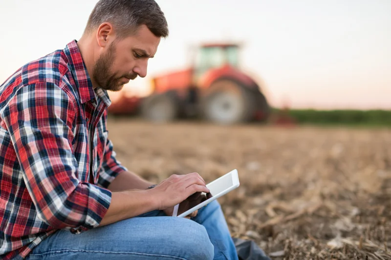 Farmer using tablet in field with tractor in background