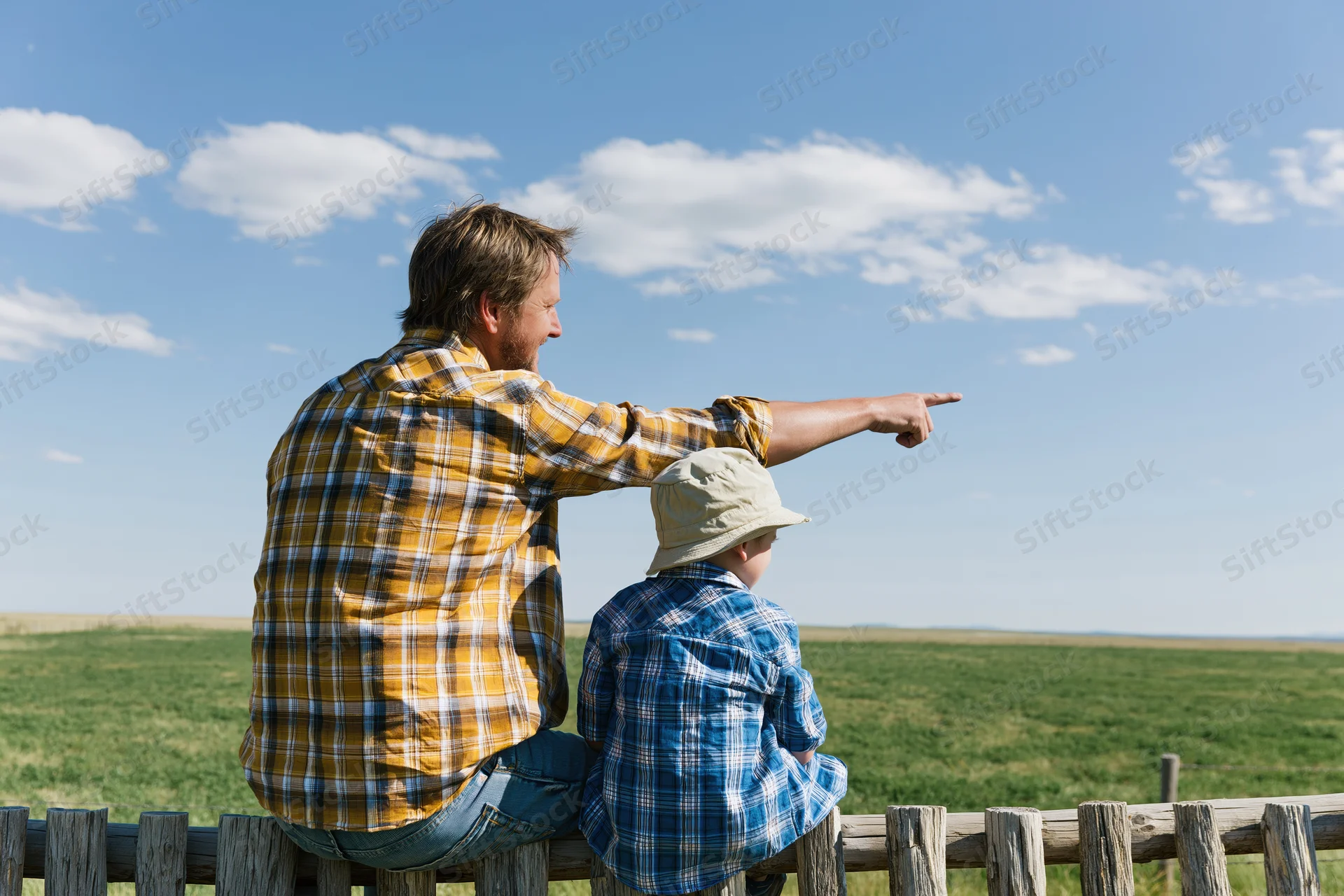 Father and son sitting on a wooden fence pointing at the countryside landscape