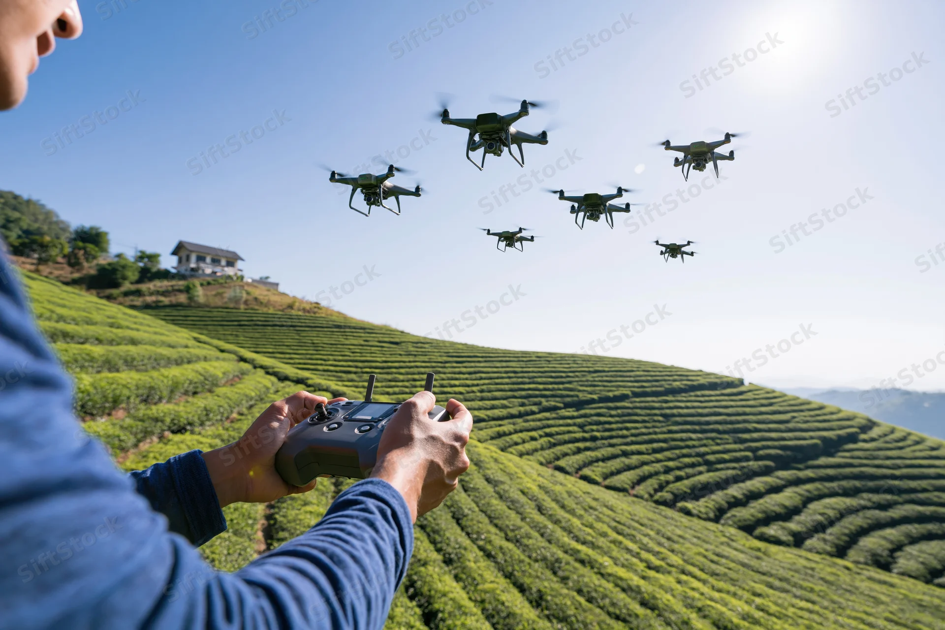 Man operating drone fleet over terraced tea plantation with remote control in hand