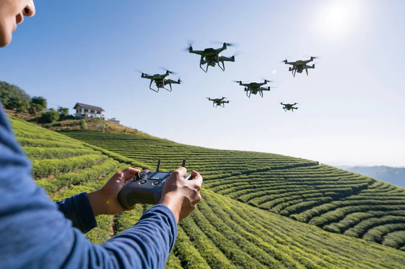 Man operating drone fleet over terraced tea plantation with remote control in hand
