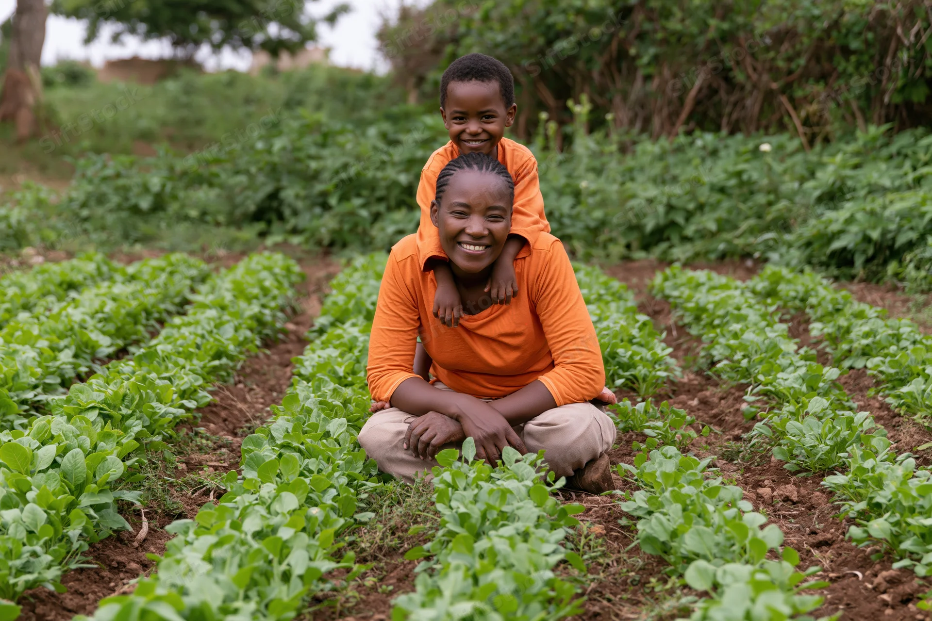 Woman kneeling in vegetable garden with child on her shoulders, smiling