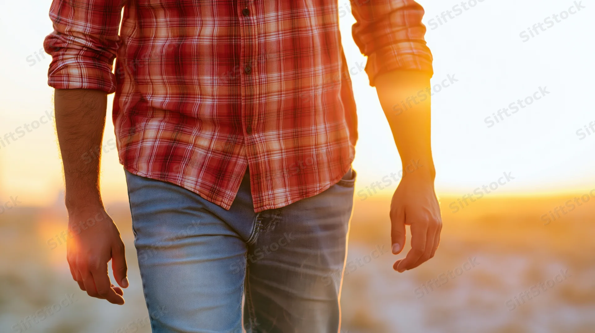 Man walking outdoors at sunset wearing red plaid shirt and jeans