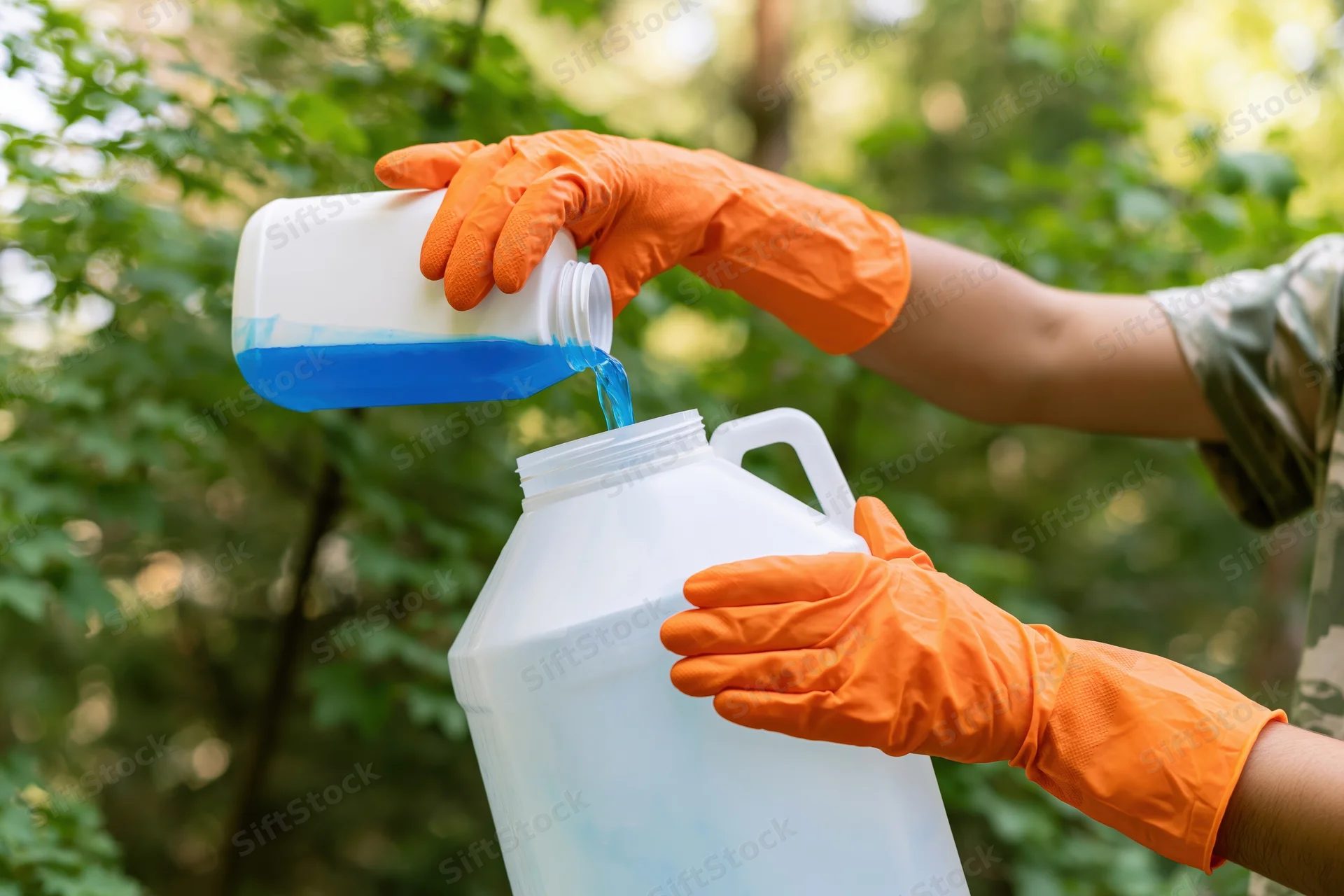 Woman in orange gloves pouring blue liquid from a bottle into a white jug outdoors in a garden