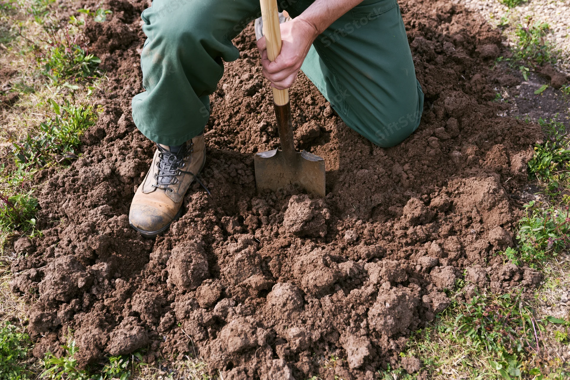 Person kneeling and digging soil with shovel in garden