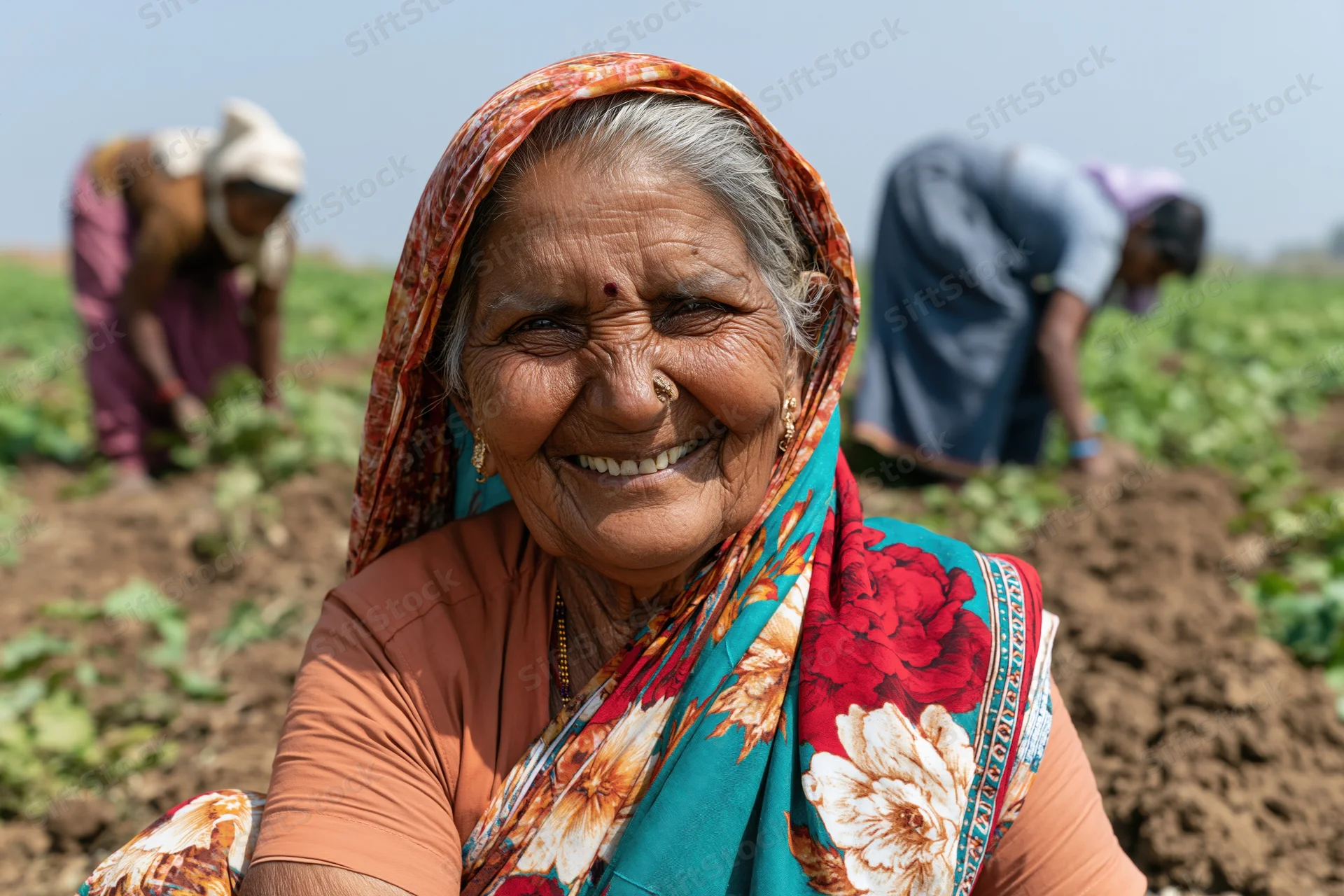 Smiling senior woman in a field with other farmers tending crops
