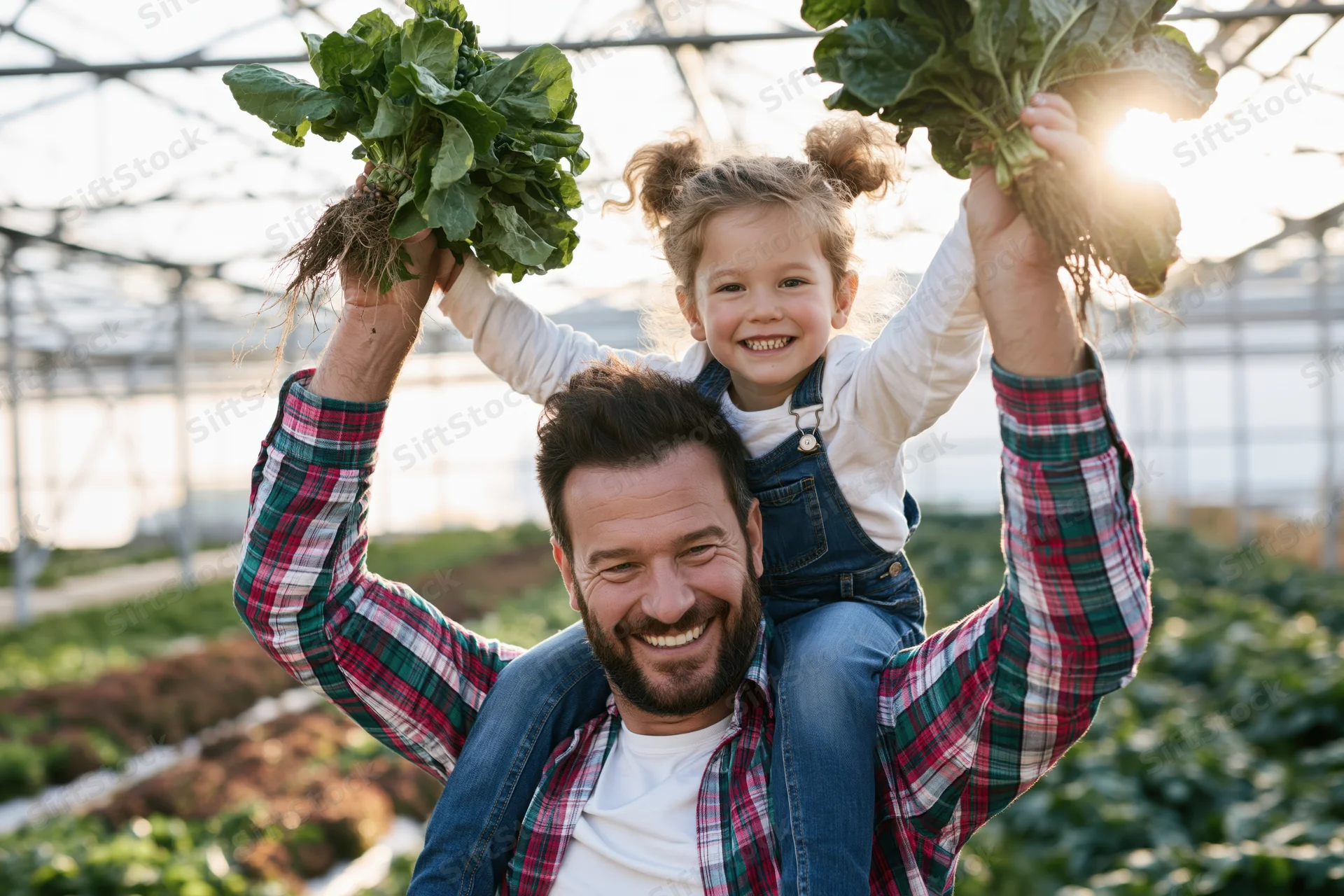 Father carrying daughter on shoulders in greenhouse holding fresh vegetables