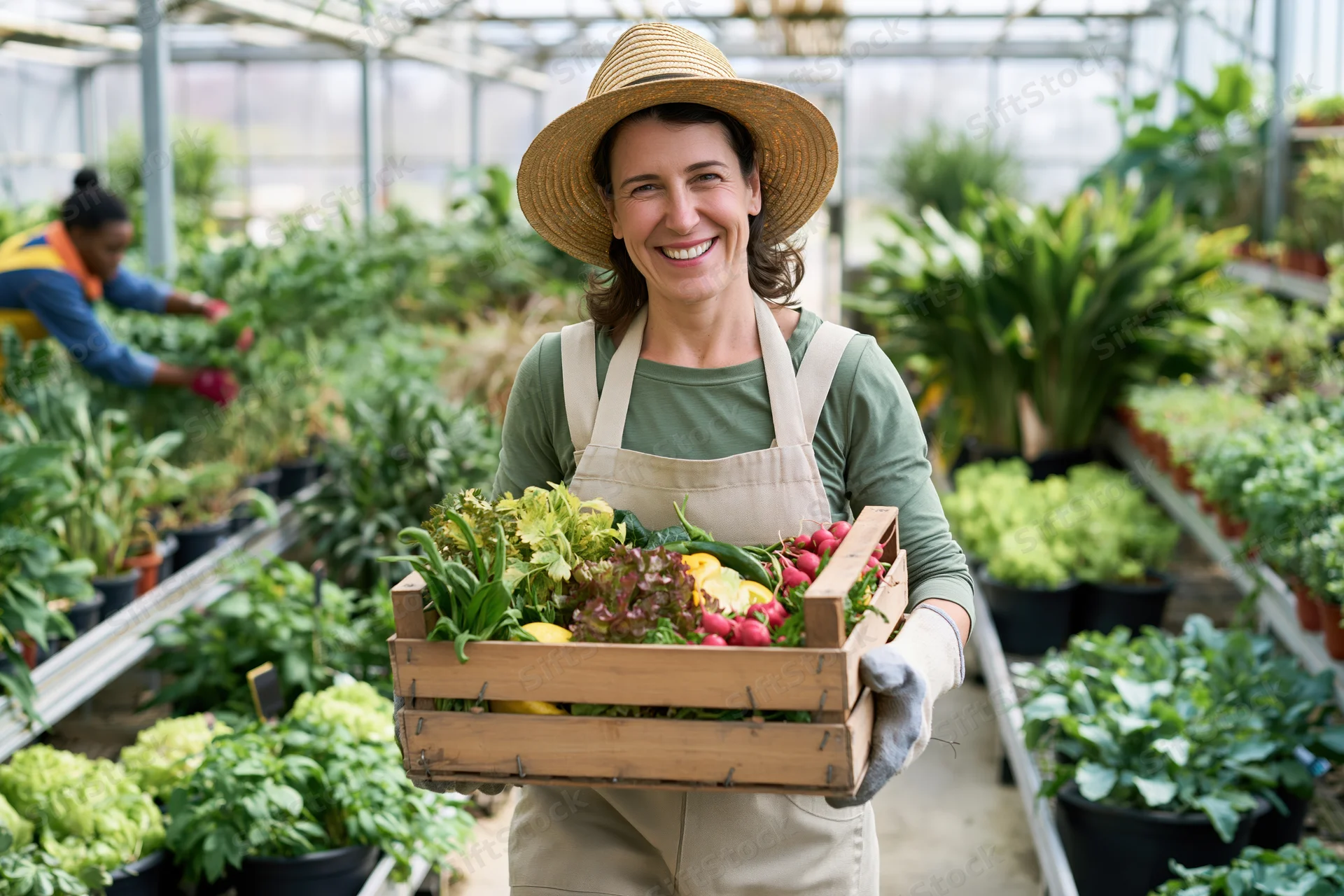 Smiling woman holding wooden crate of fresh vegetables in greenhouse