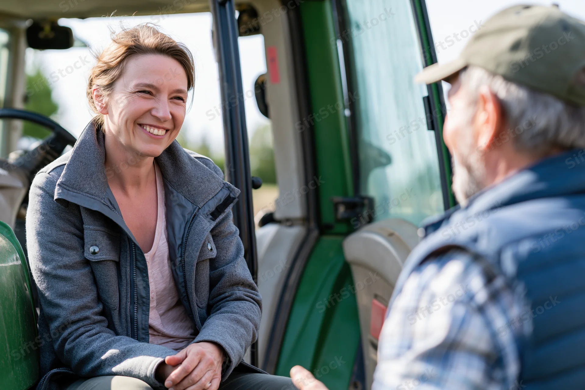 Woman smiling while sitting in tractor cab talking to man outdoors