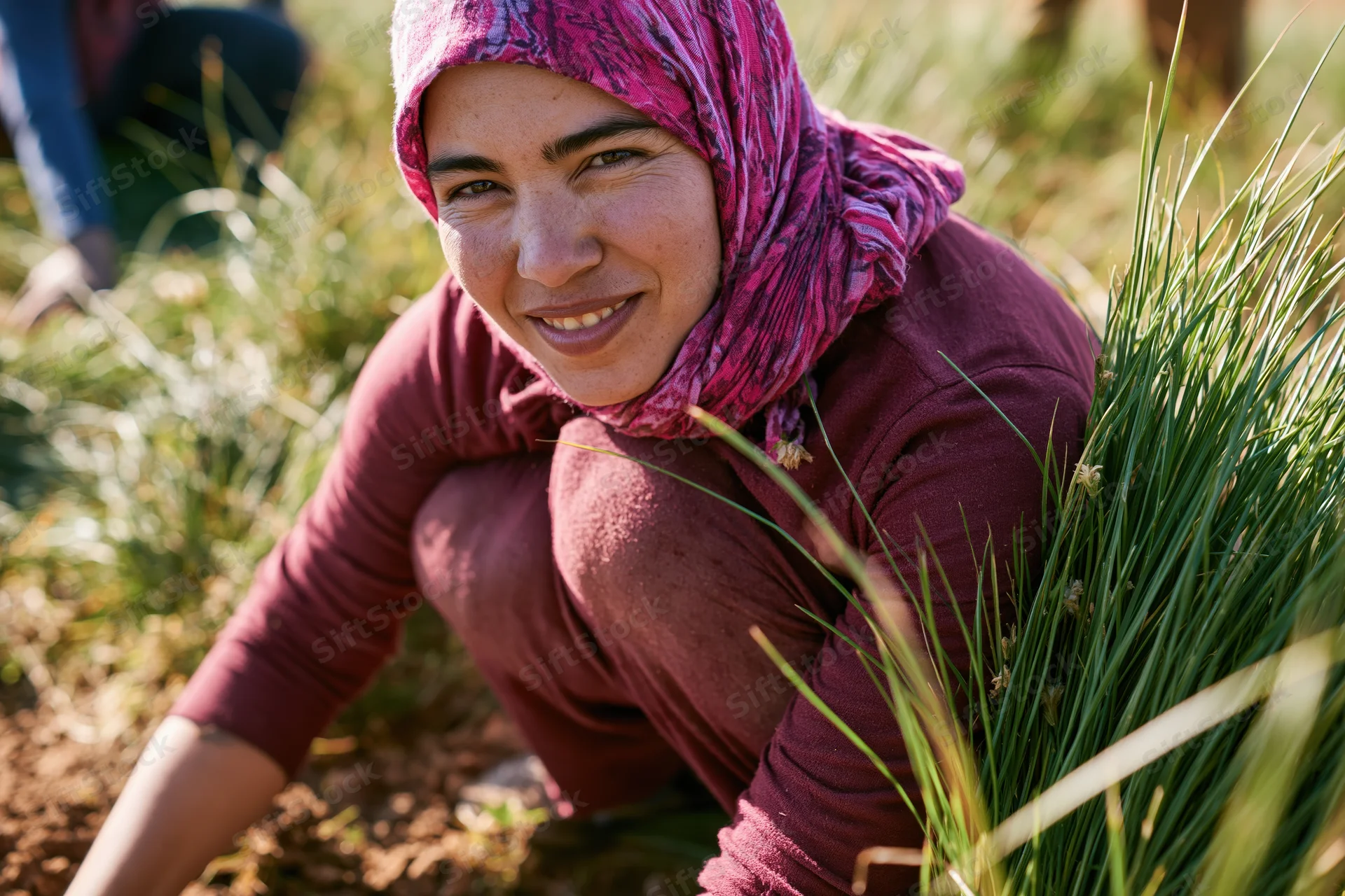 Woman crouching in a garden tending plants with a smile
