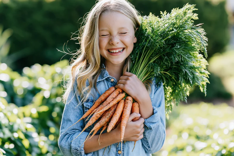 Young girl smiling while holding a bundle of fresh carrots in a garden