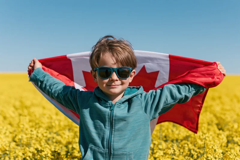 Young boy holding canadian flag in a canola field on a sunny day