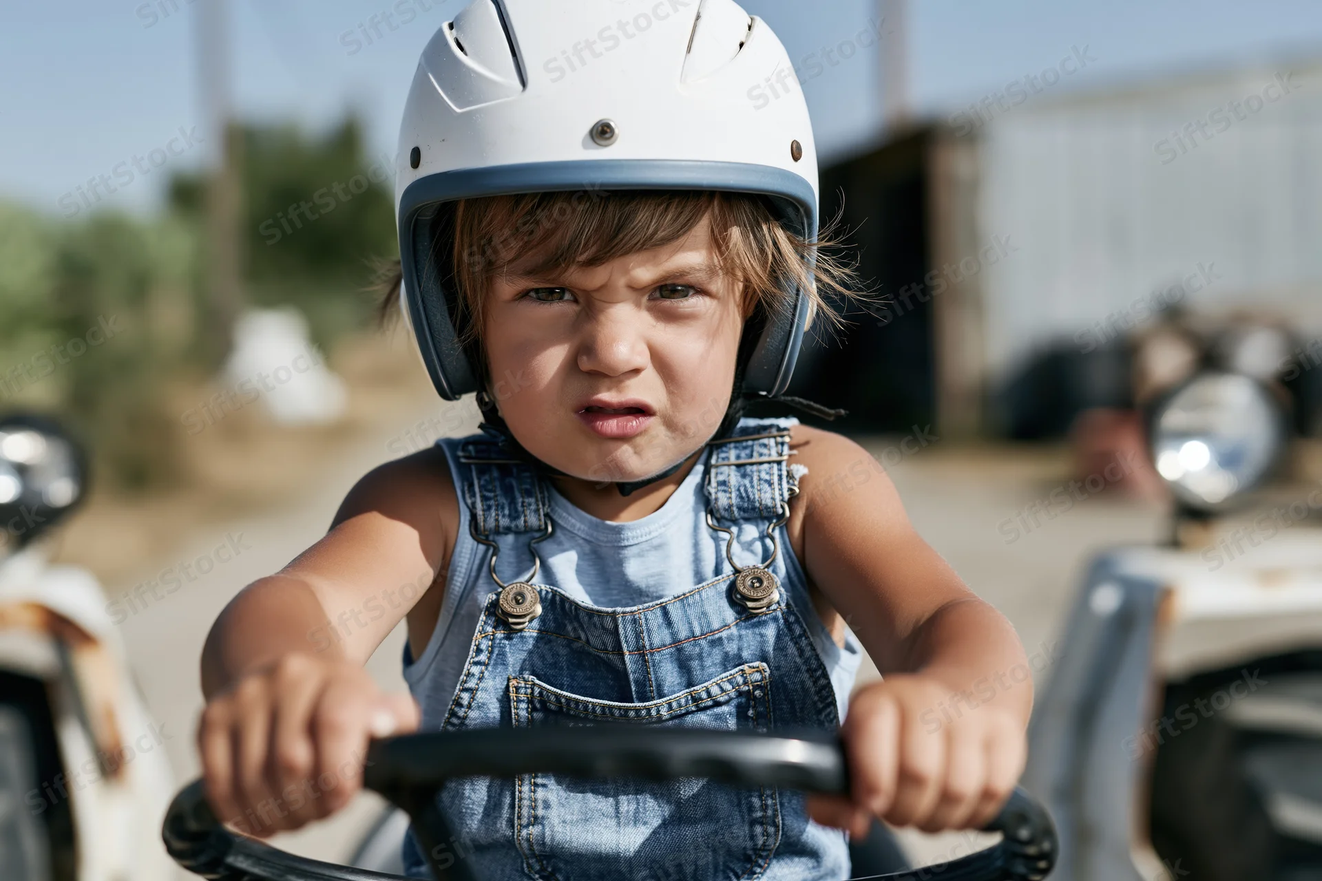 Child wearing white helmet gripping steering wheel of toy vehicle outdoors