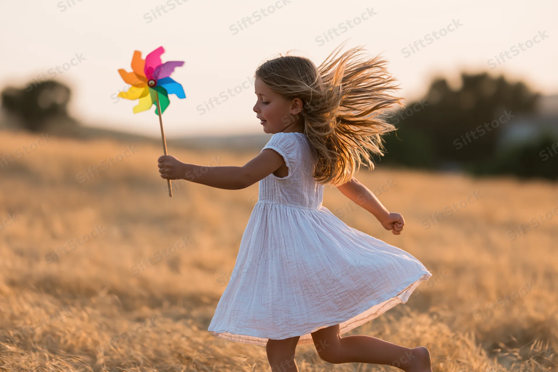 Young girl running through a golden field holding a colorful pinwheel at sunset