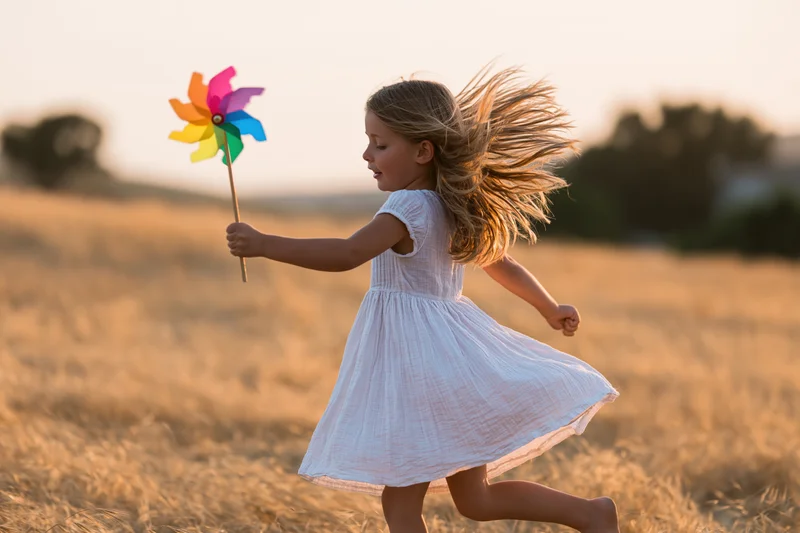 Young girl running through a golden field holding a colorful pinwheel at sunset