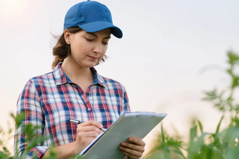 Woman writing on clipboard in a field surrounded by crops