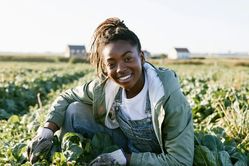 Young black woman smiling while tending leafy vegetables in a rural field
