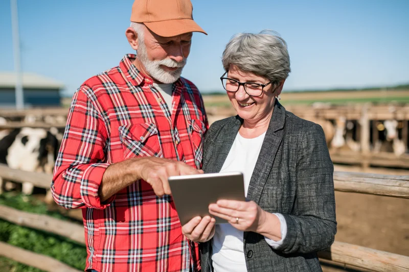Farmer and woman reviewing tablet together at a dairy farm fence
